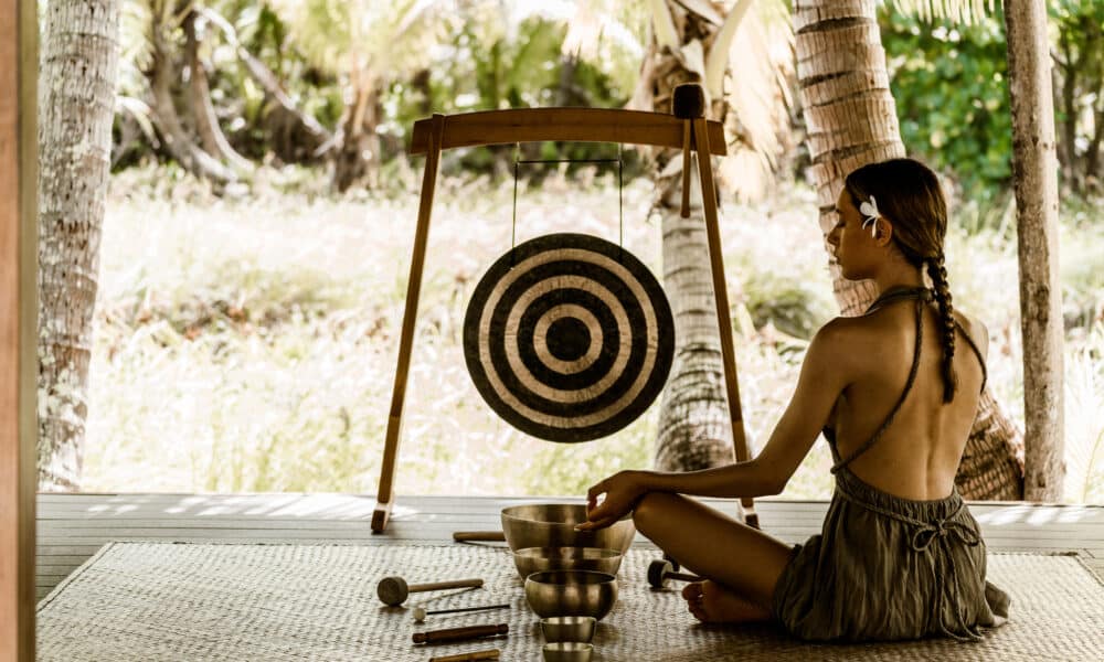 Klangschalenmeditation im Varua Te Ora Polynesian Spa des The Brando Resorts auf Tetiaroa – eine Therapeutin spielt tibetische Klangschalen und einen Gong in einem offenen Pavillon unter Palmen