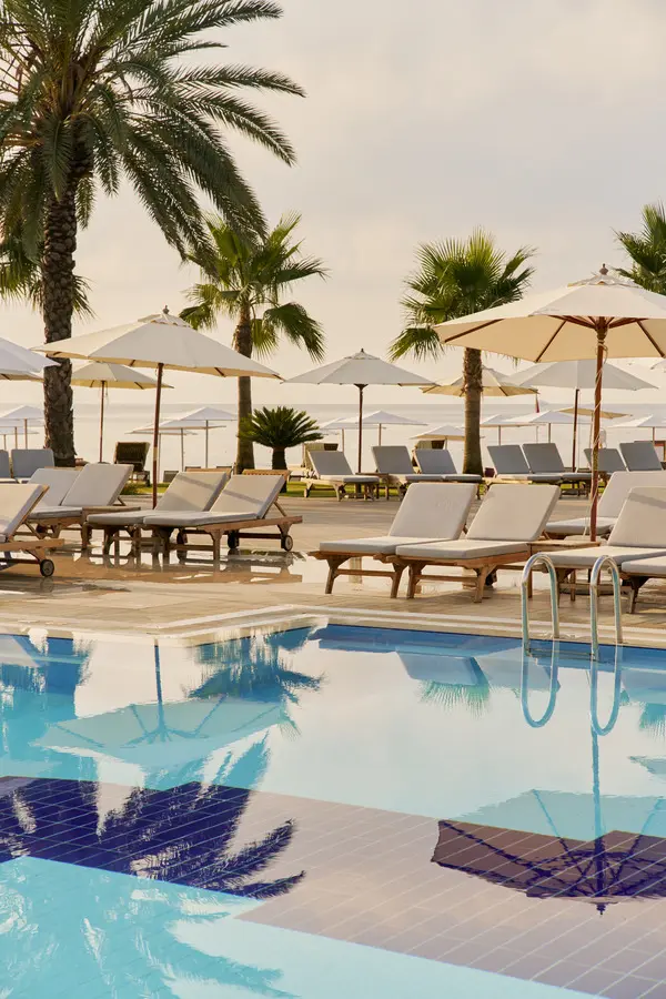 Schönste Hotelpools 2026: 6 spektakuläre Luxus-Pools für den Sommer Weisse Sonnenschirme und hochgewachsene Palmen spiegeln sich in der weitläufigen Poollandschaft des Club Med Palmiye.