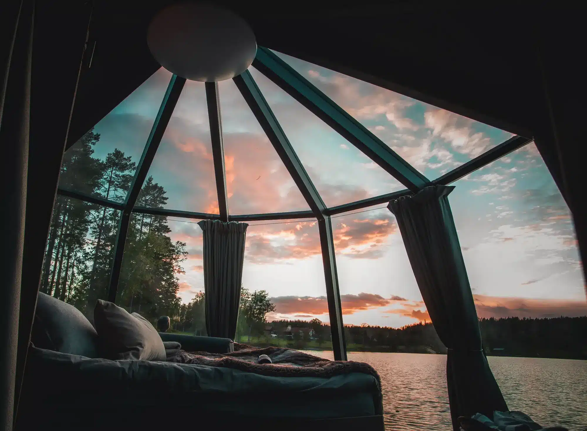 Glamping Värmland: 6 exklusive Wildnis-Erlebnisse in Schweden Das Panoramafenster der schwimmenden AuroraHut zeigt den Sonnenuntergang über den herbstlichen Gewässern von Värmland (Quelle: Visit Värmland).