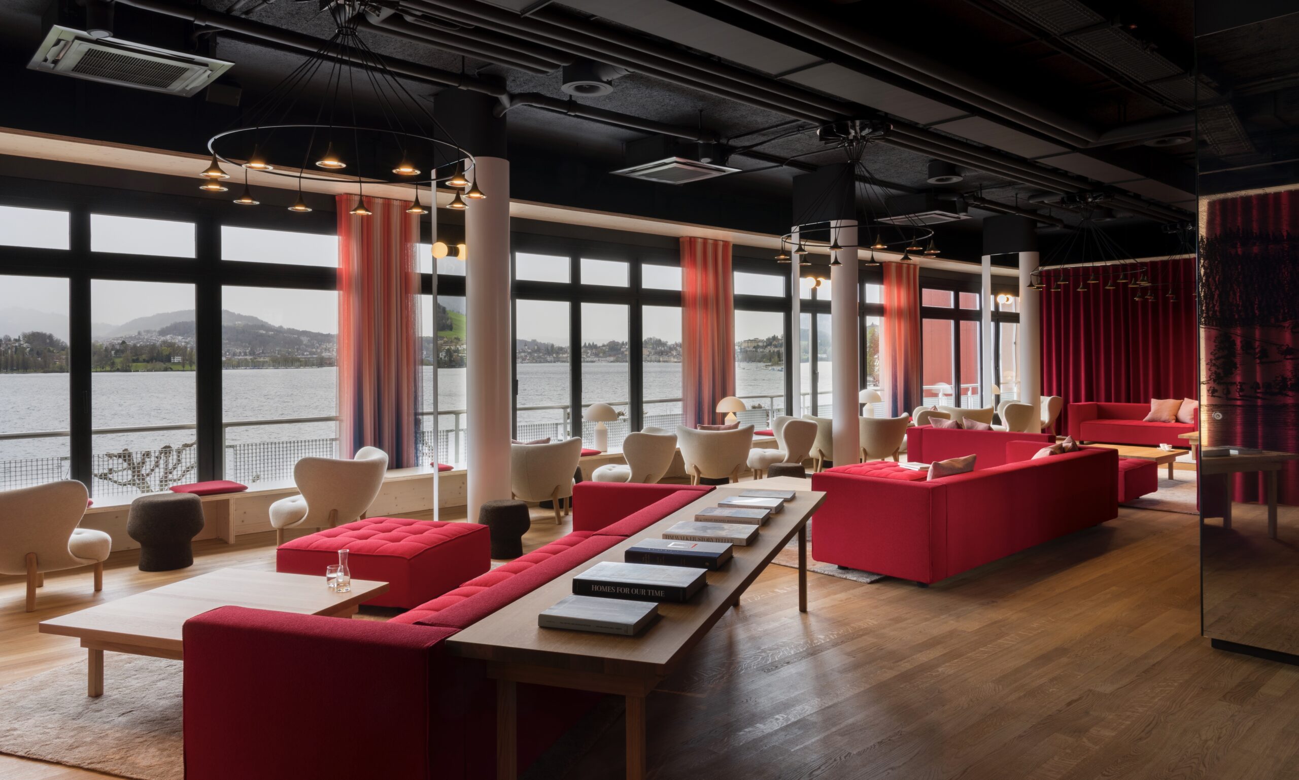 HERMITAGE Lake Lucerne: Neue Zimmer und kulinarische Neuausrichtung am Vierwaldstättersee Rote Loungemöbel und raumhohe Fenster zum See prägen die neu gestaltete Lobby Bar der HERMITAGE (Quelle: zvg).